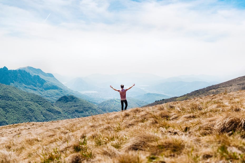 man topless standing on top of hill with dried grass field